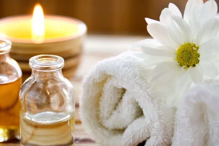 a towel with a daisy resting on top of it, with oils and a candle burning in the background