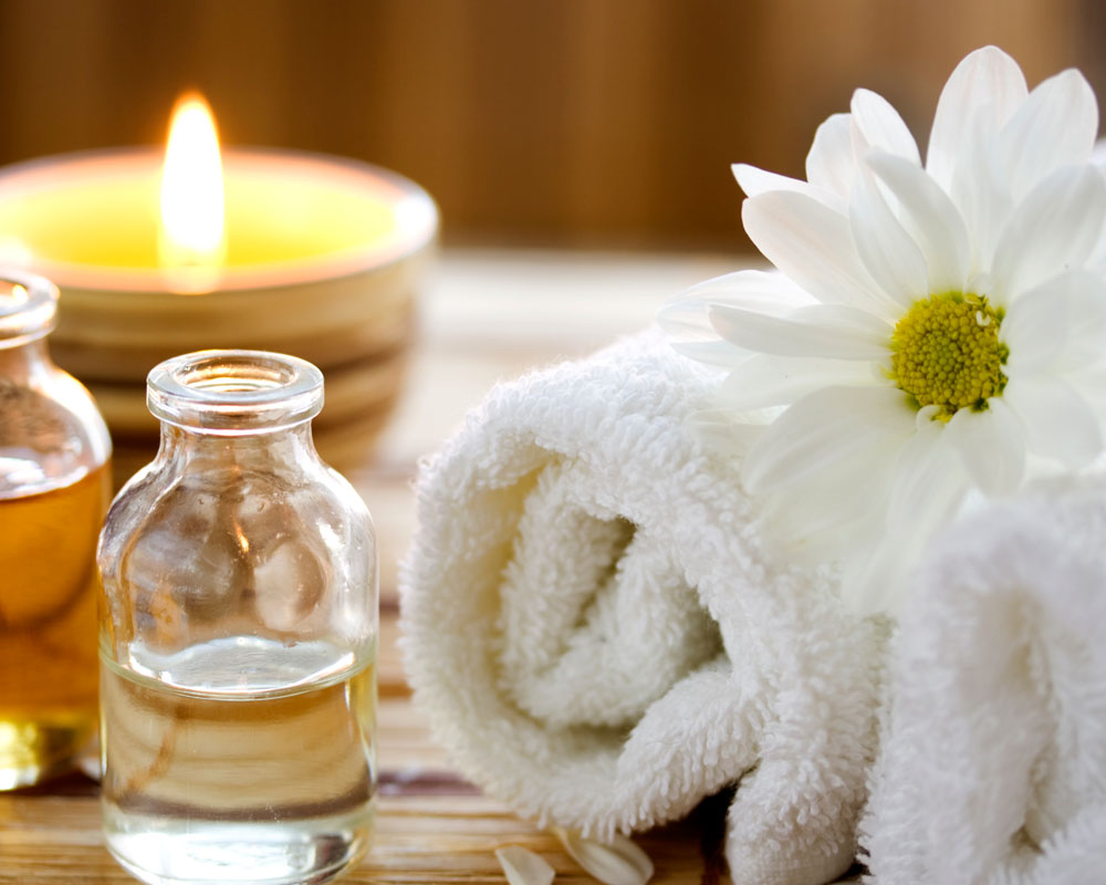 a towel with a daisy resting on top of it, with oils and a candle burning in the background