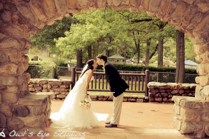 a newly married couple leaning in to kiss under a stone arch